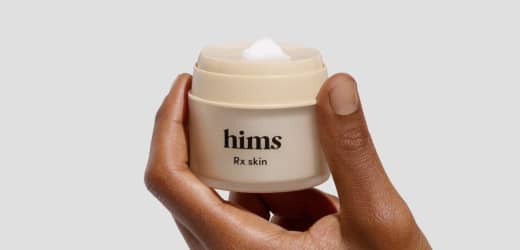 Hand holding an opened container of skincare cream